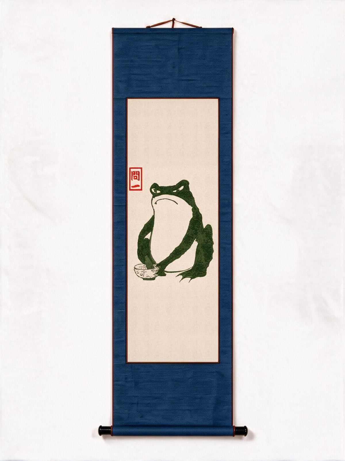 A vertical Japanese-style hanging scroll artwork on a white background. The scroll has a dark blue border and a central beige panel featuring a green frog illustration with a small red seal.
