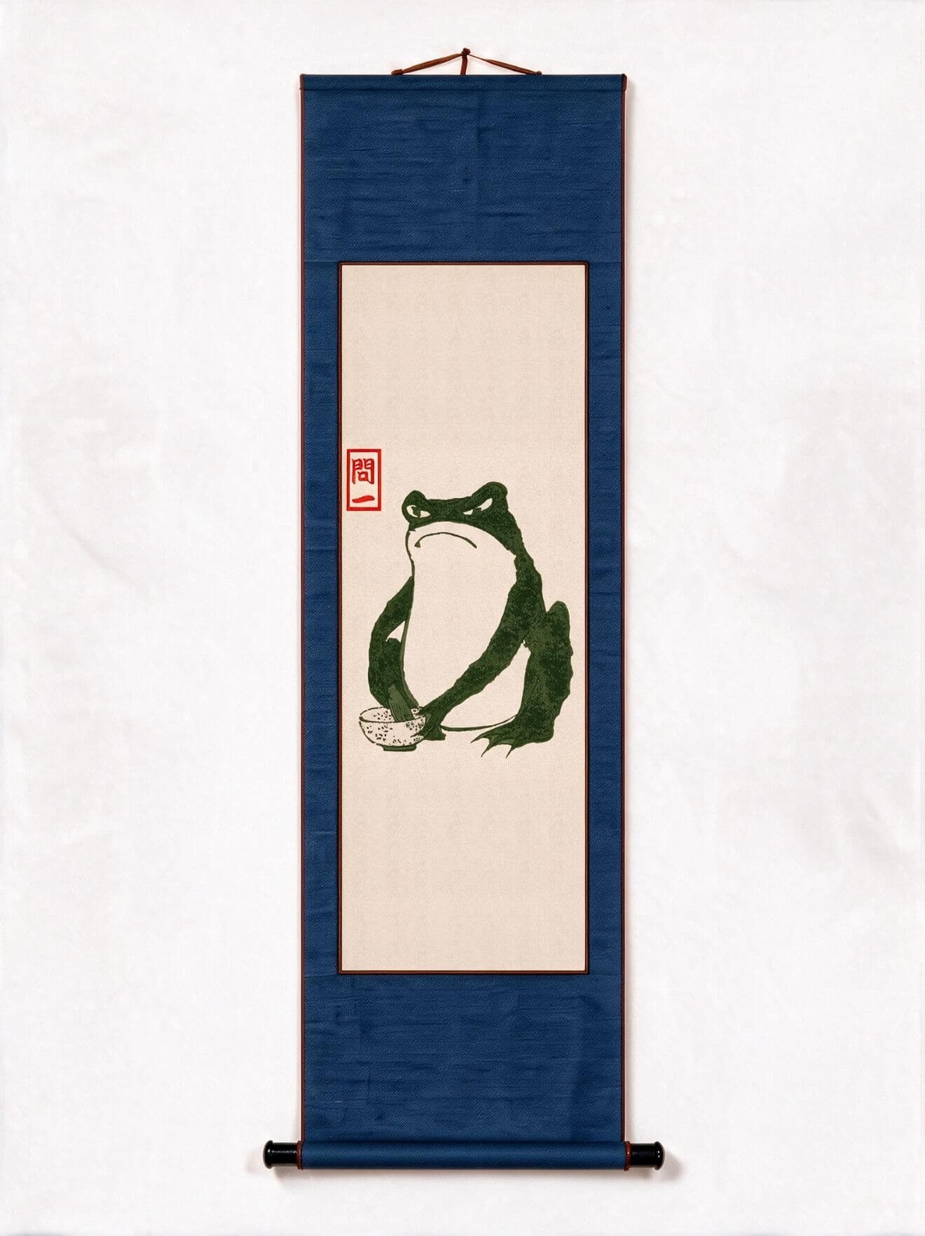 A vertical Japanese-style hanging scroll artwork on a white background. The scroll has a dark blue border and a central beige panel featuring a green frog illustration with a small red seal.