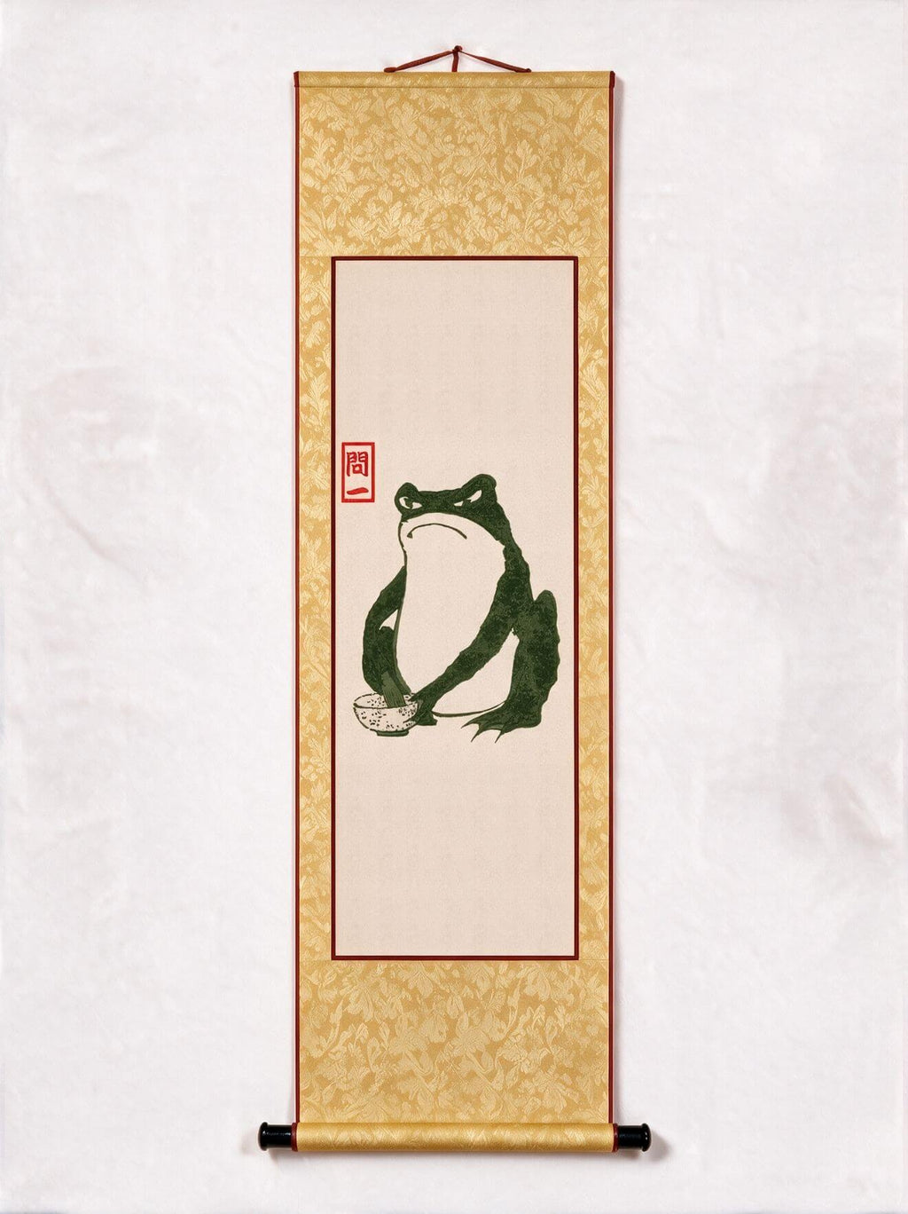 A traditional Japanese-style hanging scroll wall art featuring a green frog illustration on a beige center panel, surrounded by a gold patterned border with red accents and black hanging rods.
